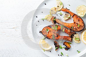 Grilled salmon steak with lemon spices and lime in a white plate on a light wooden table. Deliciously cooked salmon fillet