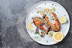 Grilled salmon steak with lemon spices and lime in a white plate on a stone slate table. Deliciously cooked salmon fillet