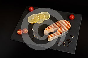 Grilled salmon steak with a lemon, tomatoes and salad on a slate plate.