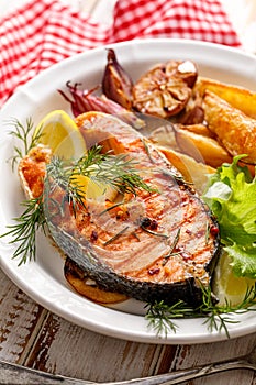 Grilled salmon steak, a portion of grilled salmon with fresh lettuce and potato wedges on a white ceramic plate on a wooden rustic