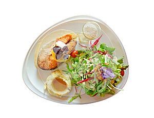 Grilled salmon steak sliced on white plate with mixed vegetable salad, mashed potatoes, topping in a glass, food in dish