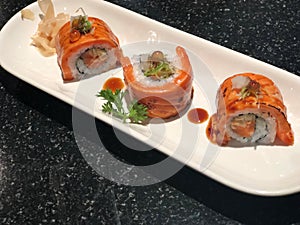 Grilled Salmon Sushi Rolls in white plate on the black bubble table,