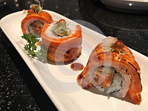 Grilled Salmon Sushi Rolls in white plate on the black bubble table,