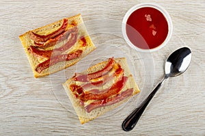 Grilled sandwiches from bread with sausages and cheese, bowl with ketchup, spoon on table. Top view