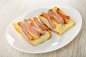 Grilled sandwiches from bread  with sausages and cheese in plate on wooden table