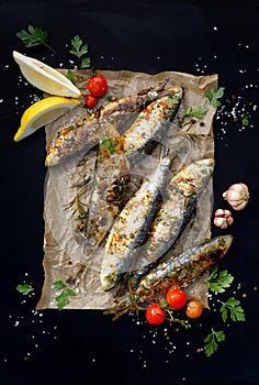 Grilled sardines on paper and a black background, top view.