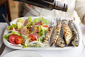 Grilled sardines with salad and olive oil on white dish
