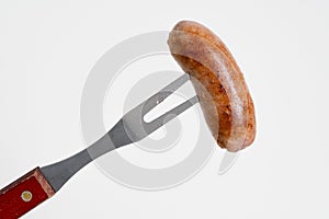 Grilled sausage on a carving fork  on white background