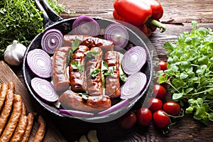 Grilled sausage with onion in a pan, raw meat and vegetables