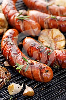 Grilled sausages with the addition of herbs and vegetables on the grill plate, outdoor, close-up