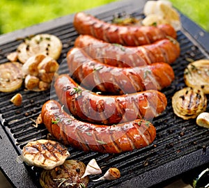 Grilled sausages with the addition of herbs and vegetables on the grill plate, outdoors.