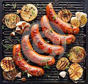 Grilled sausages with the addition of herbs and vegetables on the grill plate, top view.