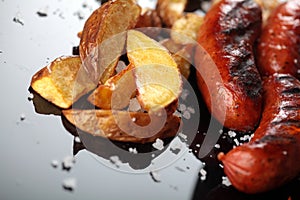 Grilled sausages.Baked potatoes .Closeup.On miroor surface.Tasty dish