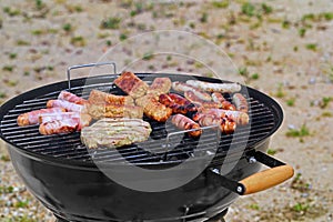 grilled sausages, cevapcici and meat on black bbq grill in the sand, grill barbecue on summer beach