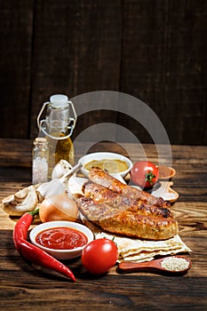 Grilled sausages, fresh vegetables, ingredients and spices on a wooden table