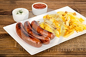 Grilled sausages and fried potatoes on the white plate on the rustic surface.
