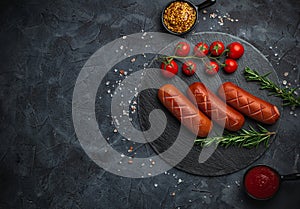 Grilled sausages with herbs, incisions, on slate stone plate round, dark background