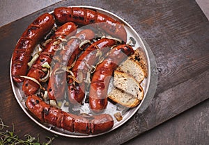 Grilled sausages with onion served with bread on a plate, on a rustic wooden cutting board. Roasted, fried meat sausages