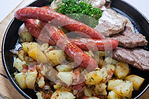 Grilled sausages with potatoes, and roasted meat on a grill pan