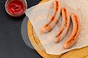 Grilled sausages with sauce ketchup on a wooden board