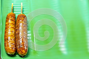 Grilled sausages on skewers, glistening with a crispy exterior, presented on vibrant green tray