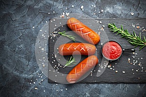 Grilled sausages with spices on a stone plate. Dark background