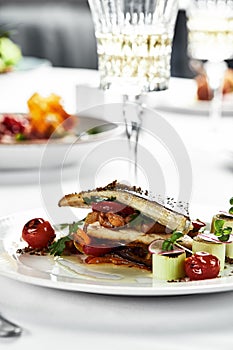 grilled sea bass with sauteed tomatoes, served with a potato ball on a white plate, sea bass fillet outline on a light