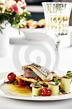 grilled sea bass with sauteed tomatoes, served with a potato ball on a white plate, sea bass fillet outline on a light