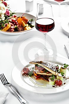 grilled sea bass with sauteed tomatoes, served with a potato ball on a white plate, sea bass fillet plan on a light