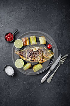 Grilled sea bream or dorado raw fish on black plate with Braised Leeks  over textured black background,  top view