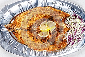 Grilled sea bream fish on foil plate served with lemon and cauliflower