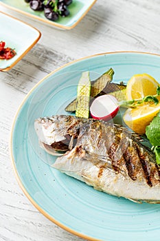 Grilled sea bream with vegetables and greens on wooden table