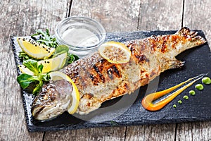 Grilled sea fish with lemon on stone slate background close up. Healthy food.