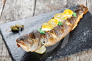 Grilled sea fish with lemon on stone slate background close up. Healthy food. Top view.