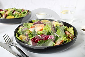 Grilled shrimp, lettuce, orange, red onion on a white plate, close-up.