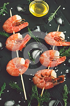 Grilled shrimp on a skewer with ice on dark backdrop. Top view