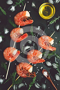 Grilled shrimp on a skewer with ice on dark backdrop. Top view seafood on plate