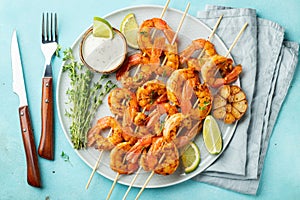 Grilled shrimp skewers or langoustines served with lime, garlic and sauce on a light blue concrete background. Seafood