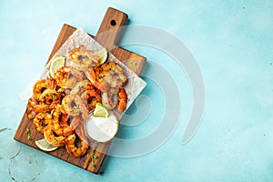 Grilled shrimp skewers or langoustines served with lime, garlic and sauce on a light blue concrete background. Seafood