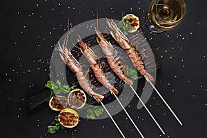 Grilled shrimp skewers. Seafood, shellfish. Shrimps Prawns skewers with herbs, garlic and lemon on black stone photo