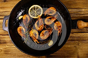 Grilled shrimp with spices, rosemary and lemon in grill frying pan on a wooden table. Top view