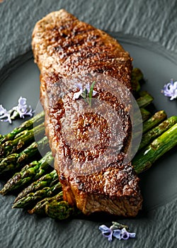 Grilled Sirloin beef steak on fried asparagus served on black slate plate with rosemary flowers