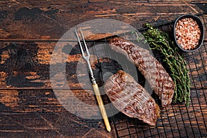 Grilled Sirloin flap or Bavette beef meat steak on a griil with herbs. Wooden background. Top view. Copy space