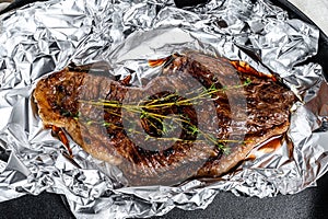 Grilled sirloin steak in foil. Black background. Top view