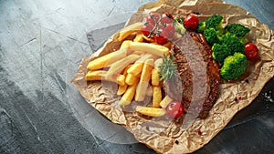 Grilled sirloin steak with potato fries, broccoli and cherry tomatoes on crumpled paper