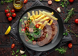 Grilled sirloin steak with potato fries and vegetables, tomato salad in a black plate. rustic table