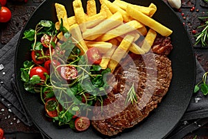 Grilled sirloin steak with potato fries and vegetables, tomato salad in a black plate. rustic table