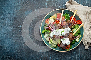 Grilled skewer meat beef kebabs on sticks served with fresh vegetables salad on plate on rustic concrete background from