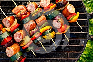 Grilled skewers of meat, sausages and various vegetables on a grill plate, outdoors, top view.