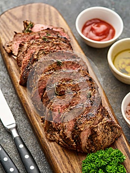 Grilled sliced beef steak on cutting board over grey table. Chuck tenderloin steak